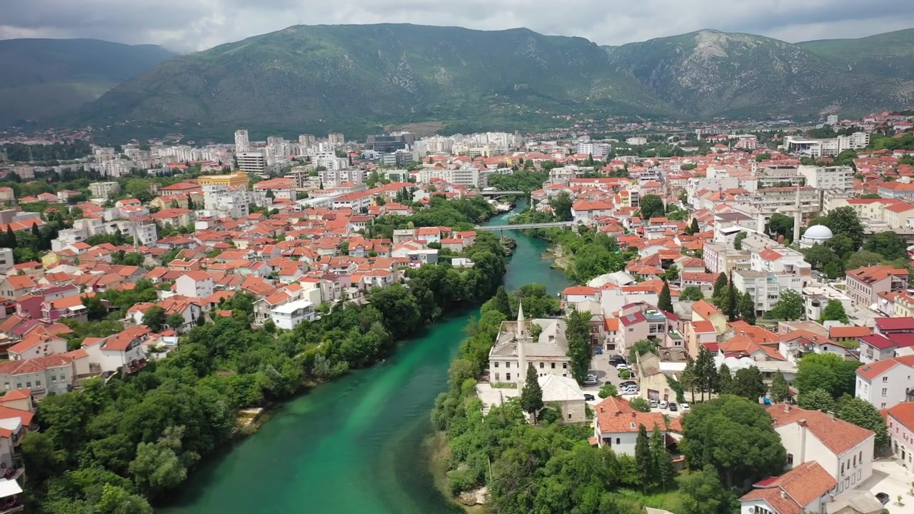 Dechberoucí široký záběr dronem na historický Stari Most (Starý most) přes smaragdovou řeku Neretvu v Mostaru, Bosna a Hercegovina. Zahrnuje tradiční osmanskou architekturu a turisty