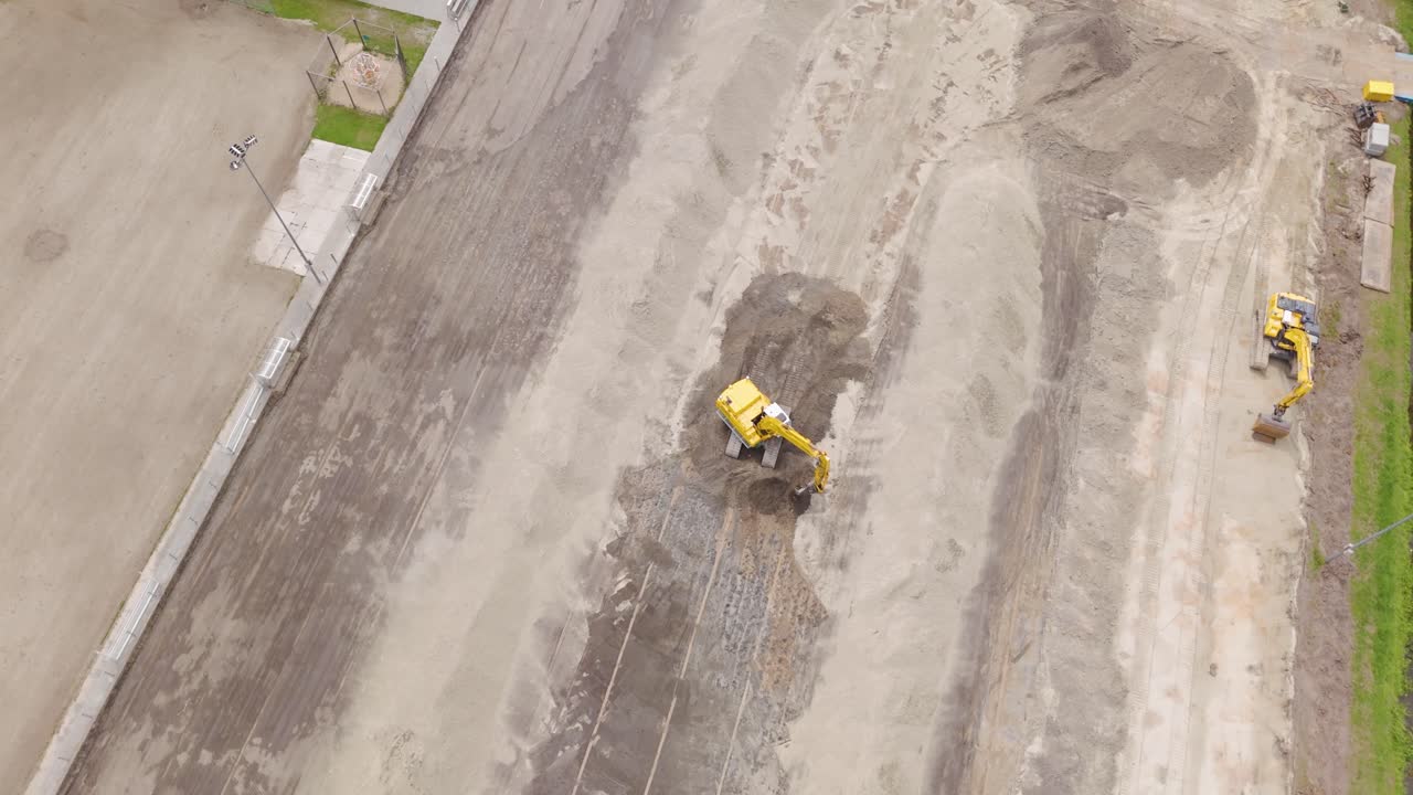 Wide drone shot showing multiple excavators working together to prepare a sports field for grass installation