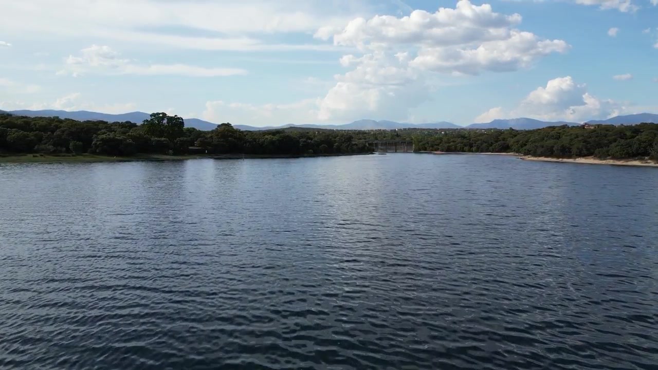 Lievi increspature sul bacino di Valmayor con uno sfondo di montagne lontane sotto un cielo parzialmente nuvoloso. Perfetto per documentari sulla natura o progetti ambientali.