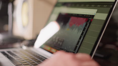 primer plano de una pantalla de computadora que muestra software de producción de audio, con una mano operando un ratón. proceso activo de edición o producción de música o sonido, con un monitor de estudio borroso en el fondo