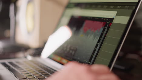 close-up of a computer screen displaying audio production software, with a hand operating a mouse.active process of editing or producing music or sound, with a studio monitor blurred in the background