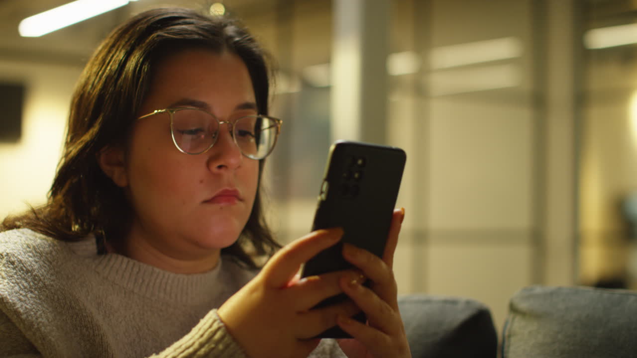 mujer joven pasando la noche en casa sentada en el sofá con el teléfono móvil desplazándose por internet o redes sociales 3