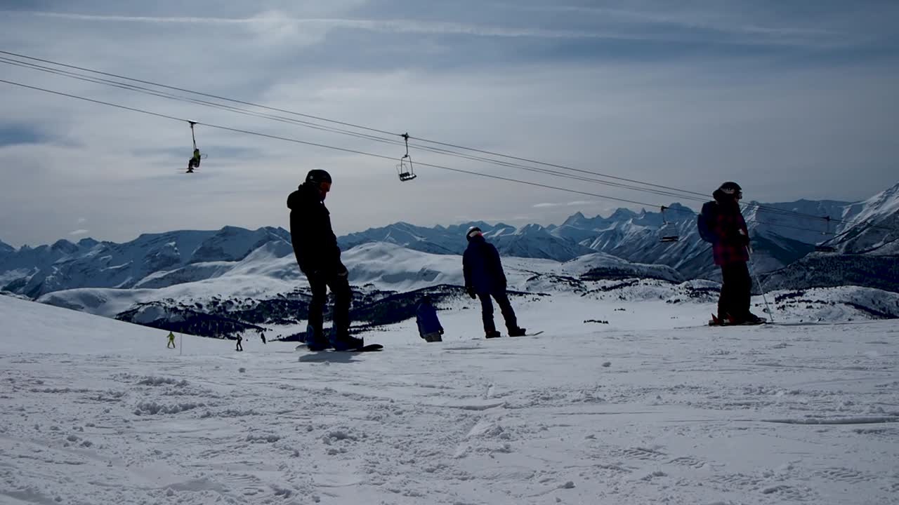 스노우 보더는 의자 리프트를 배경으로 눈 덮인 산에 있는 스키 리조트에서 움직이기 시작합니다.
