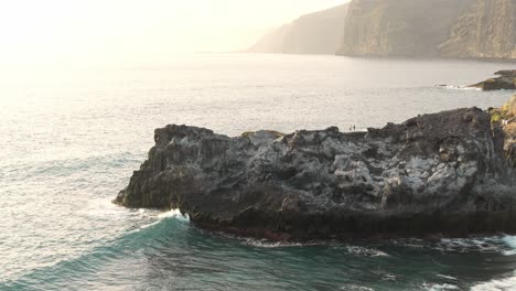 Ocean-waves-in-slow-motion-washing-rocky-cliff,-bright-sunlight-in-background