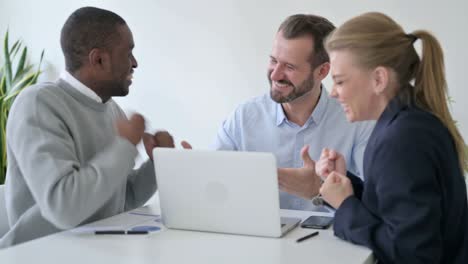 mixed race business people celebrating success while using laptop in office