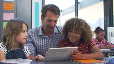 maestro usando una tableta con dos niños en clase primaria