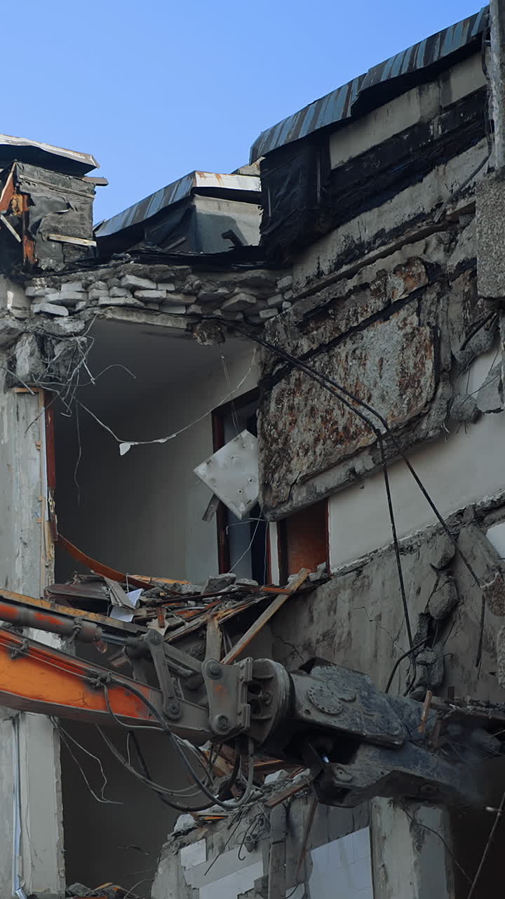 Ruins of the building under blue sky being demolished by the excavator machine. Disrupted house under the process of demolition for future city development. Vertical video