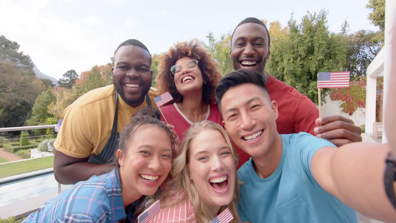 Happy diverse group of friends holding flags of usa and taking selfie in garden, slow motion