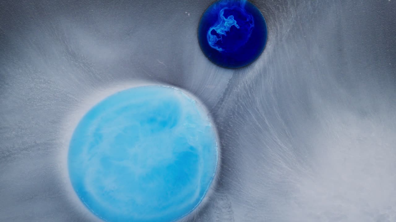 Two blue ink drops merge and swirl in milky fluid, creating dreamy abstract patterns