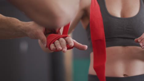 mid section of male trainer wrapping boxing tape on hands of female boxer at the gym