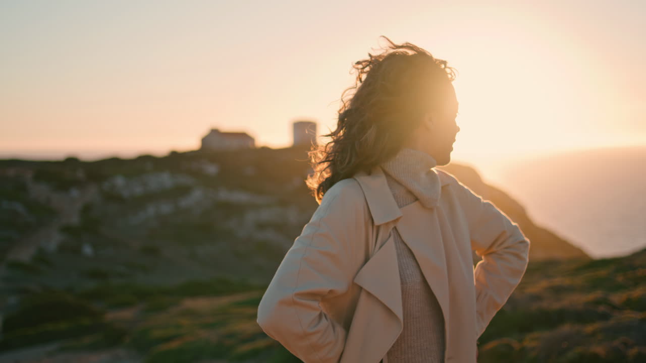 Cheerful traveler enjoying evening on seaside hill. Happy girl posing at ocean