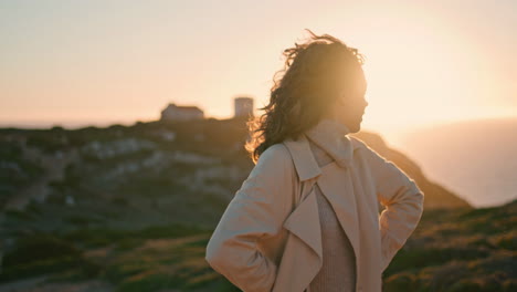 Cheerful-traveler-enjoying-evening-on-seaside-hill.-Happy-girl-posing-at-ocean