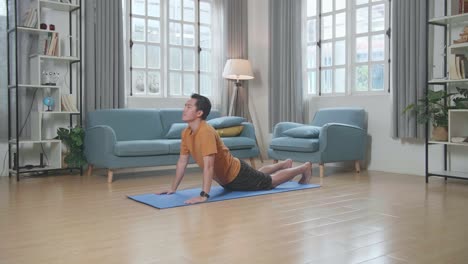 hombre asiático haciendo yoga mirando hacia arriba al perro en la alfombra en casa
