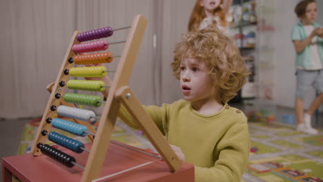 little boy playing with a panel moving wooden pieces in classroom in a montessori school