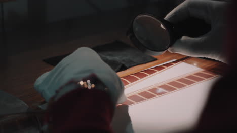 a man with white gloves working at a film studio examines a film on special analog equipment