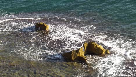 blue ocean waves break over reef with large rocks, slow motion