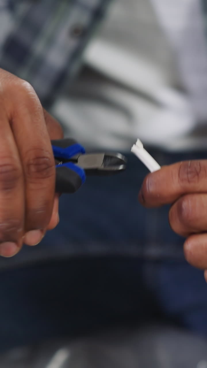Black repairman cuts insulation of cable sitting on sofa with plastic foil in apartment closeup. African-American worker operates with wire in house