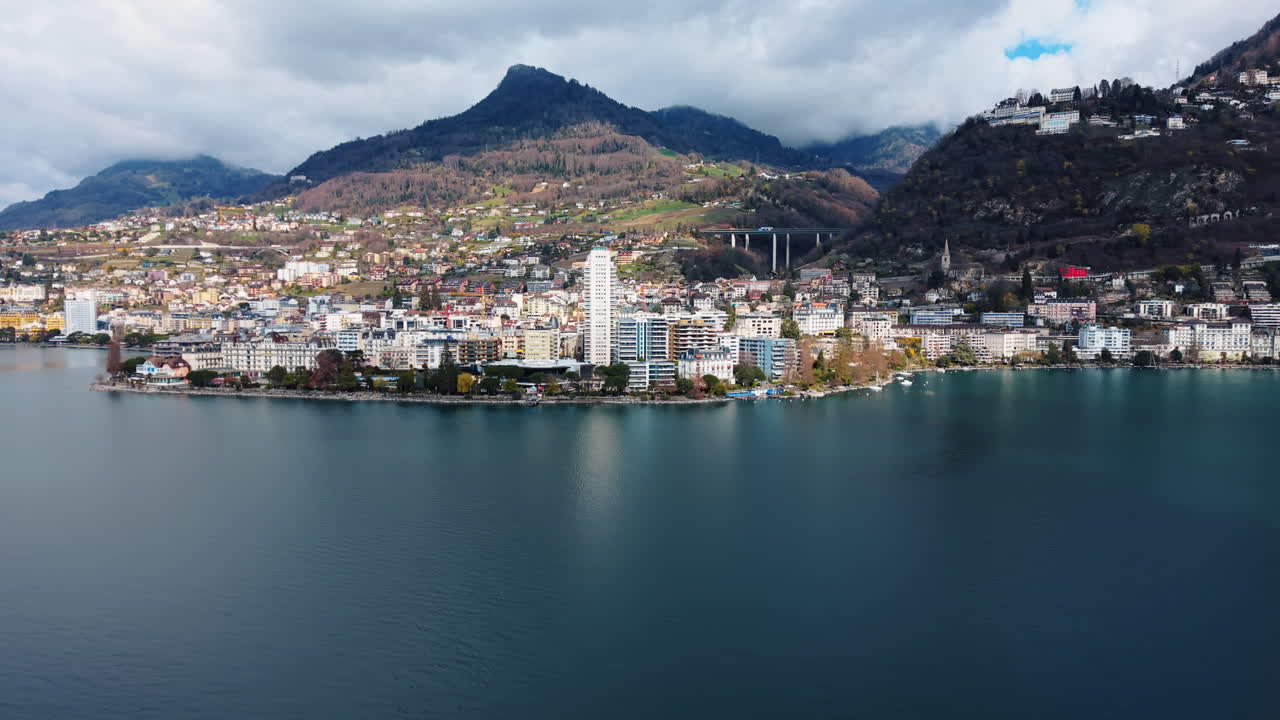 Aerea: Lago di Ginevra, panorama urbano di Montreux e montagne di giorno nel Canton Vaud, Svizzera, ripresa orbitale con drone.