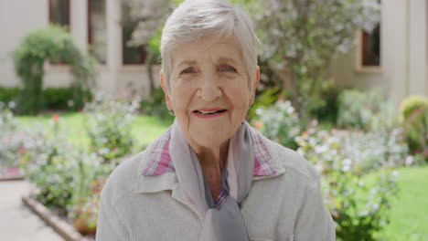 portrait of elderly woman smiling happy looking at camera enjoying sunny day in beautiful garden background