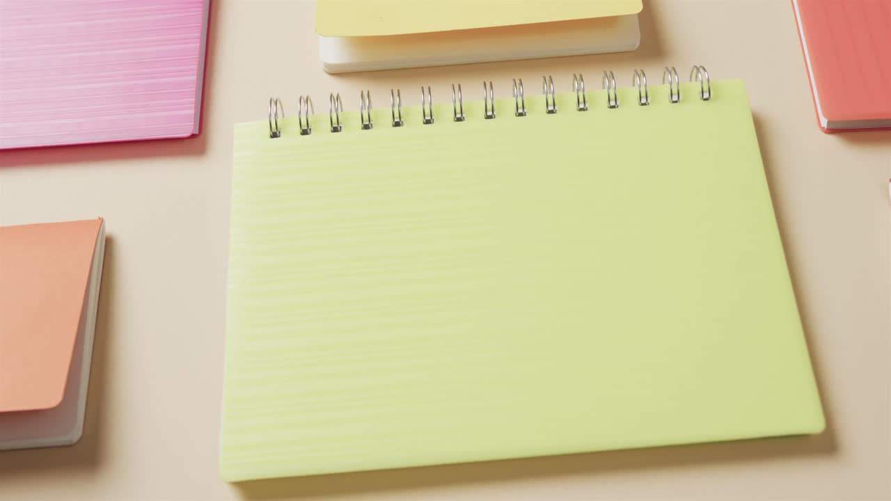 Close up of colourful notebooks arranged on beige background, in slow motion