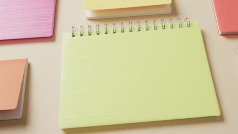 Primer-Plano-De-Coloridos-Cuadernos-Dispuestos-Sobre-Fondo-Beige,-En-Cámara-Lenta