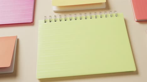 close up of colourful notebooks arranged on beige background, in slow motion