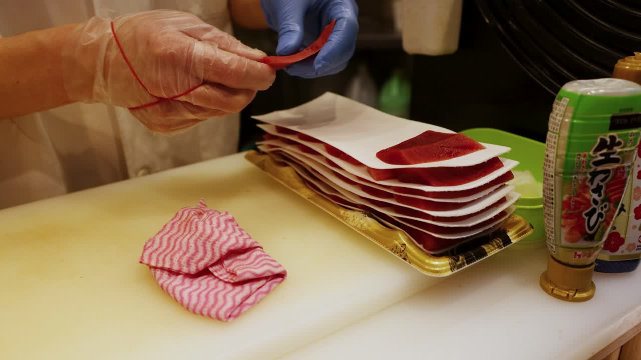 Primo piano di uno chef con i guanti che dispone fette di tonno fresco su un tagliere bianco