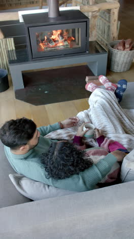 vertical video of biracial couple embracing on sofa in front of fireplace at home, slow motion