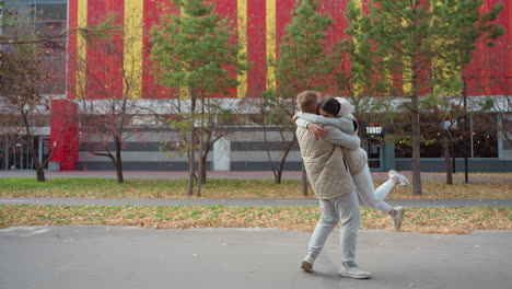joyful moment as siblings in matching casual outfits embrace with open arms, smiling warmly while man gently turns sister around amidst autumn trees and colorful building