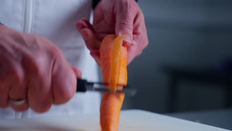 Chef-wearing-a-white-apron-peeling-a-carrot-on-a-cutting-board