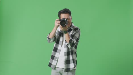 asian photographer using a camera taking picture while standing on green screen background in the studio