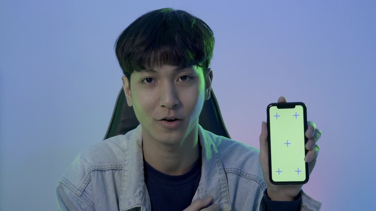 Young man gamer talking to camera at her steaming room. He showing smartphone and talk to camera.