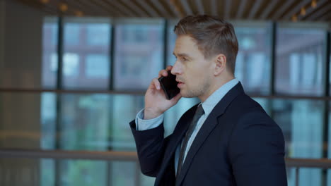 Busy Businessman Talking on Phone, Making Phone Call on the Go while Walking Along Office Corridor in Slow Motion - profile tracking shot