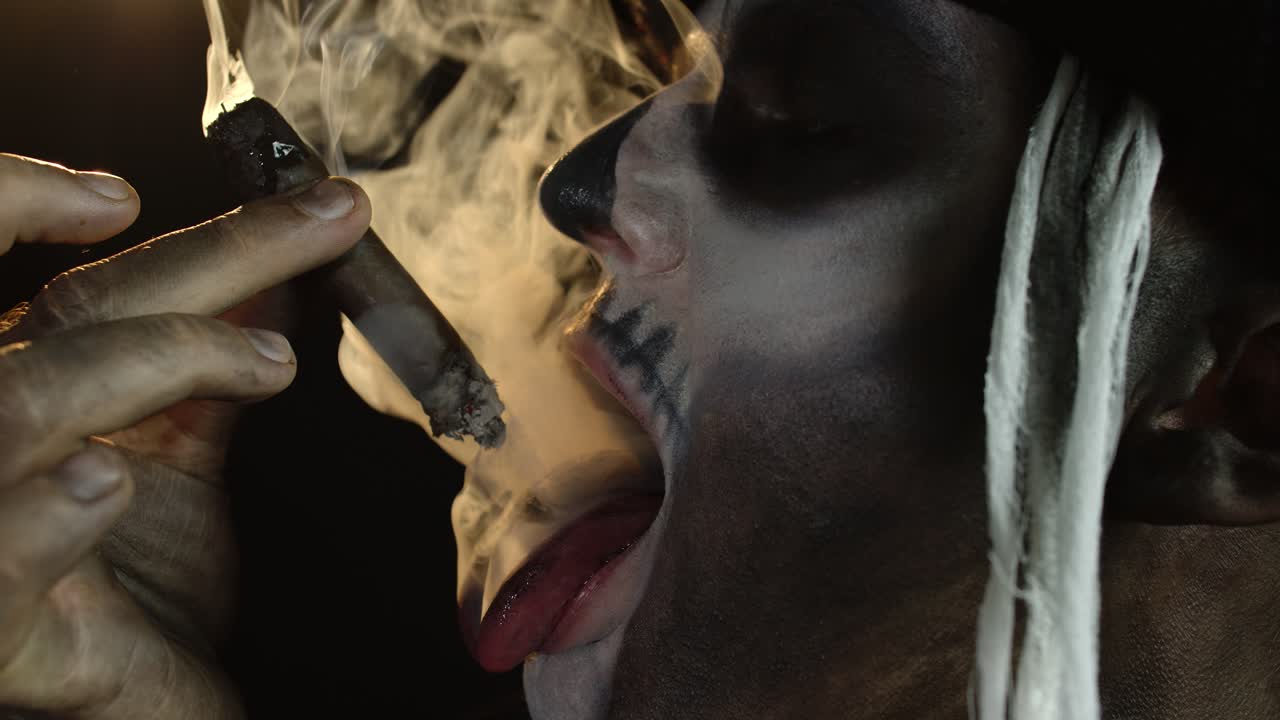 hombre aterrador en esqueleto disfraz de cosplay de halloween fumando cigarro, haciendo caras, mostrando la lengua