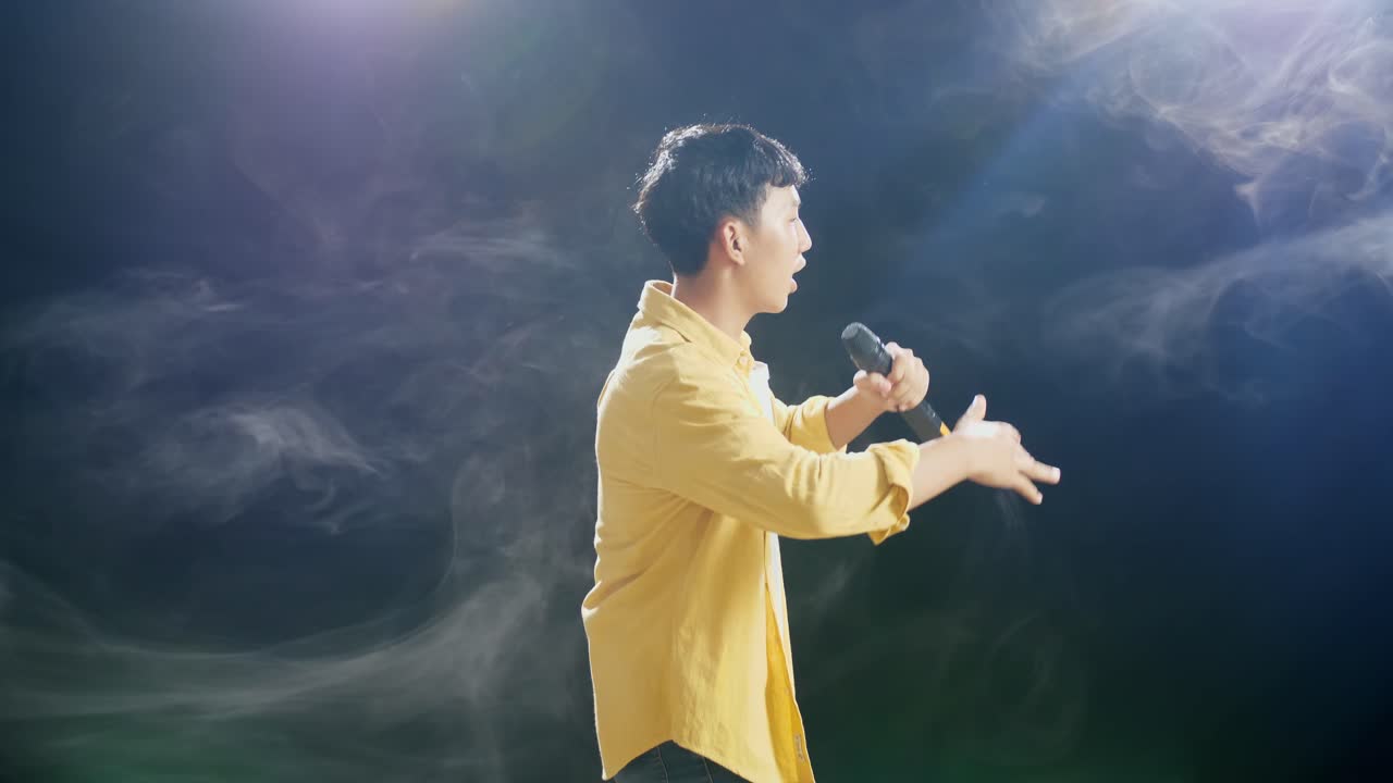 젊은 아시아 소년이 마이크를 들고 색 연기가 검은색 배경에 하는 측면 시각