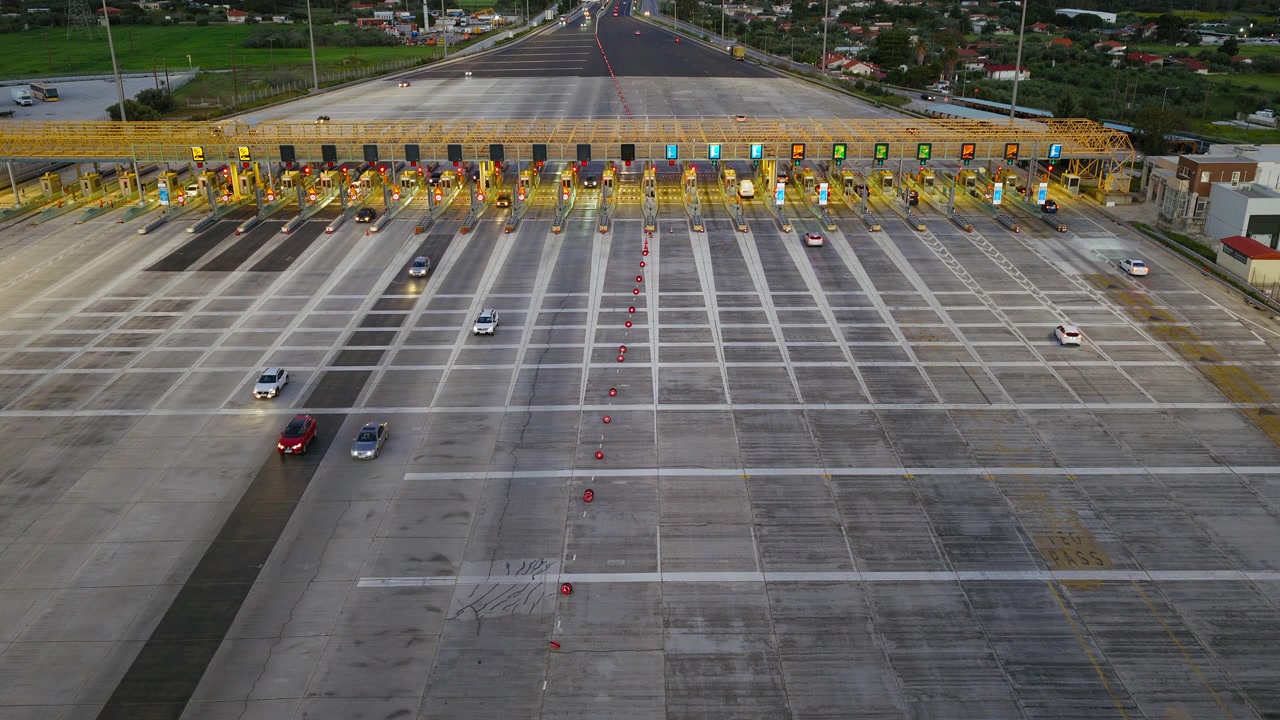 Toma estática de dron de una estación de peaje en una autopista griega. Coches haciendo cola y pasando por las cabinas. Perspectiva aérea en ángulo. Metraje de archivo de infraestructura vial.