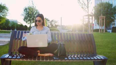 Business woman is sitting on bench outdoors and using lap top for working out office and eating salad