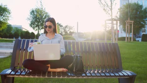 business woman is sitting on bench outdoors and using lap top for working out office and eating salad