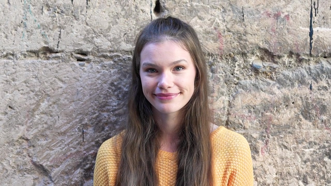 Una giovane donna posa contro un muro di pietra consumato situato in un ambiente urbano
