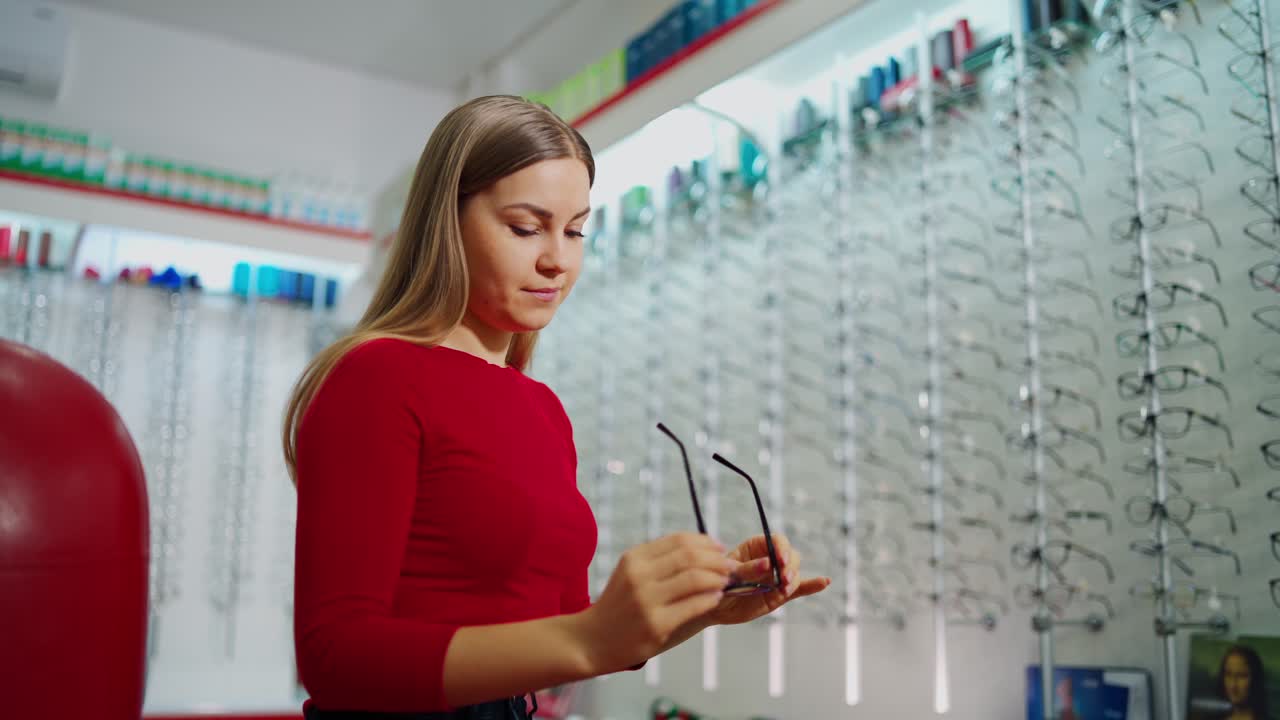 Beautiful female choosing glasses in the optical store. Young woman buyer trying on new eyeglasses. Eyesight concept.
