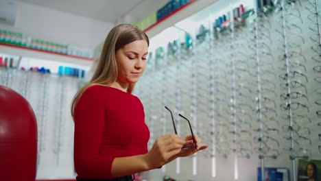 beautiful female choosing glasses in the optical store. young woman buyer trying on new eyeglasses. eyesight concept.