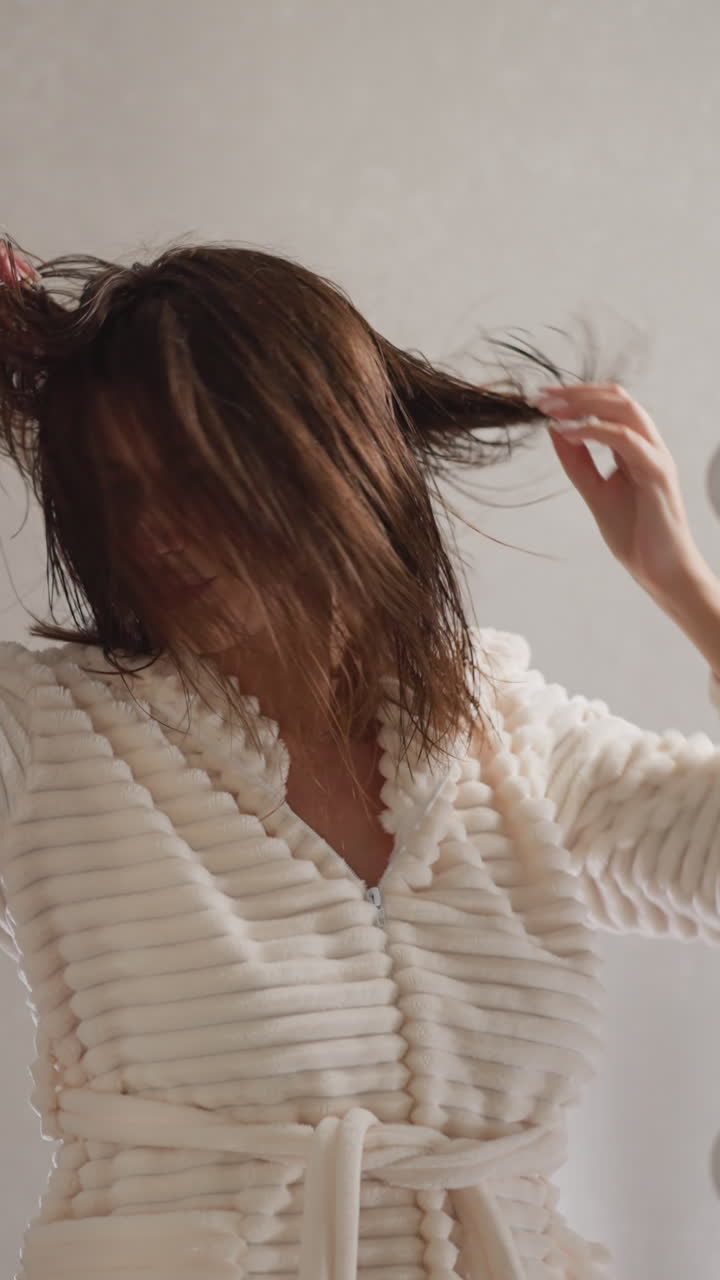 visitante femenina del salón lanza el cabello en diferentes direcciones en cámara lenta. mujer enérgica morena sacude el cabello mojado con las manos mirándose en el espejo