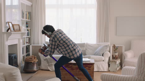 joven feliz bailando en casa usando una aspiradora celebrando el éxito escuchando música usando auriculares divirtiéndose bailando en la sala de estar el fin de semana
