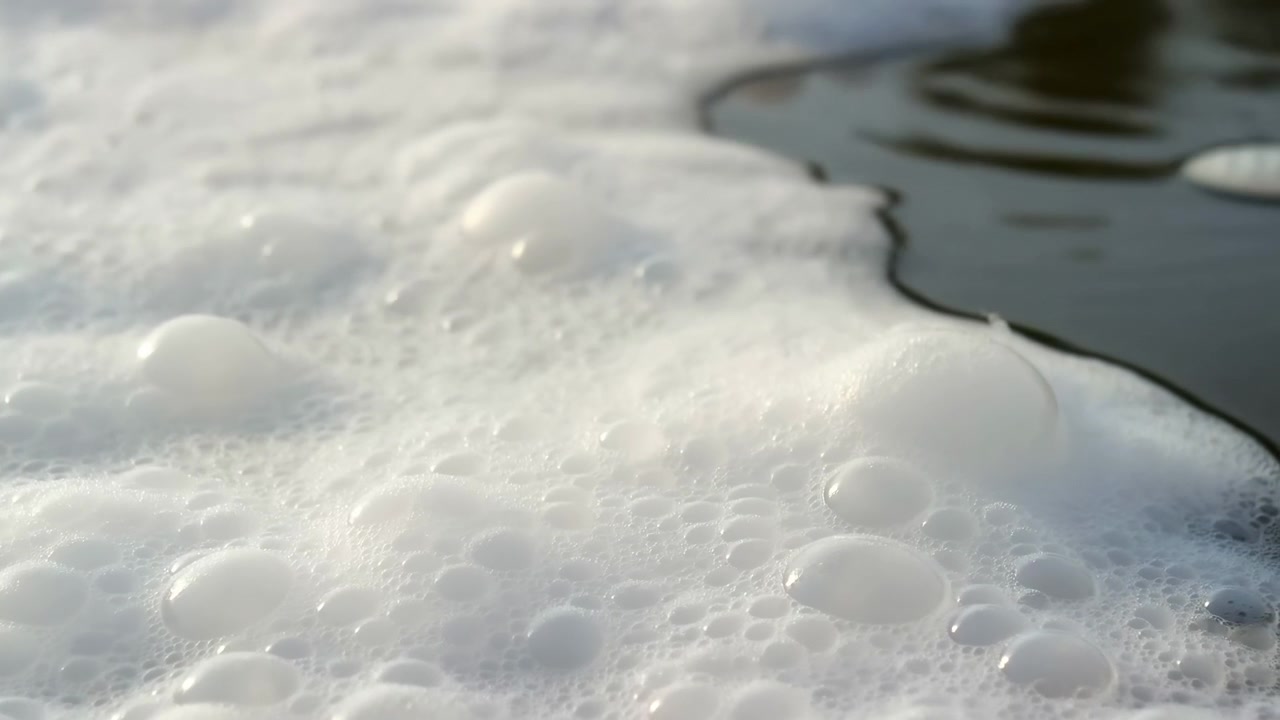 Movimento di schiuma e increspature sulla superficie dell'acqua, in primo piano. Acqua schiumosa con increspature e texture di schiuma di sapone, da una prospettiva ravvicinata dall'alto.