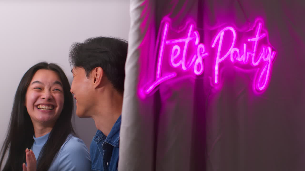 pareja o amigos divirtiéndose en una cabina de fotos con un letrero de neón "vamos a festejar" afuera