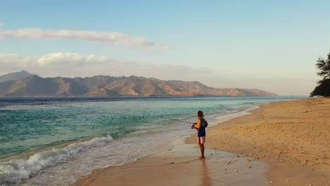 a young boy with his fishing rod went fishing at the shore of the beautiful bora bora island at sunset - wide shot