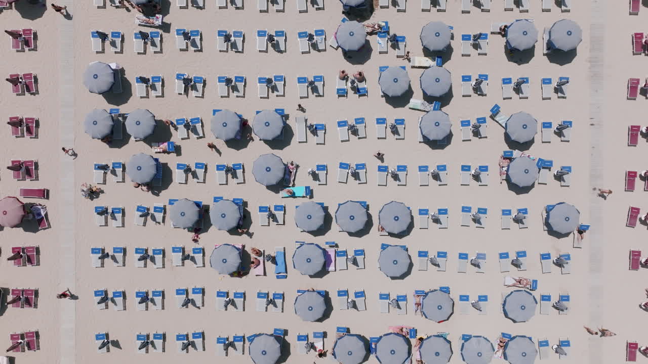 낮 동안 이탈리아 바리의 해변에 있는 파란색 우산과 파란색 의자에 있는 관광객들의 하향식 공중 영상