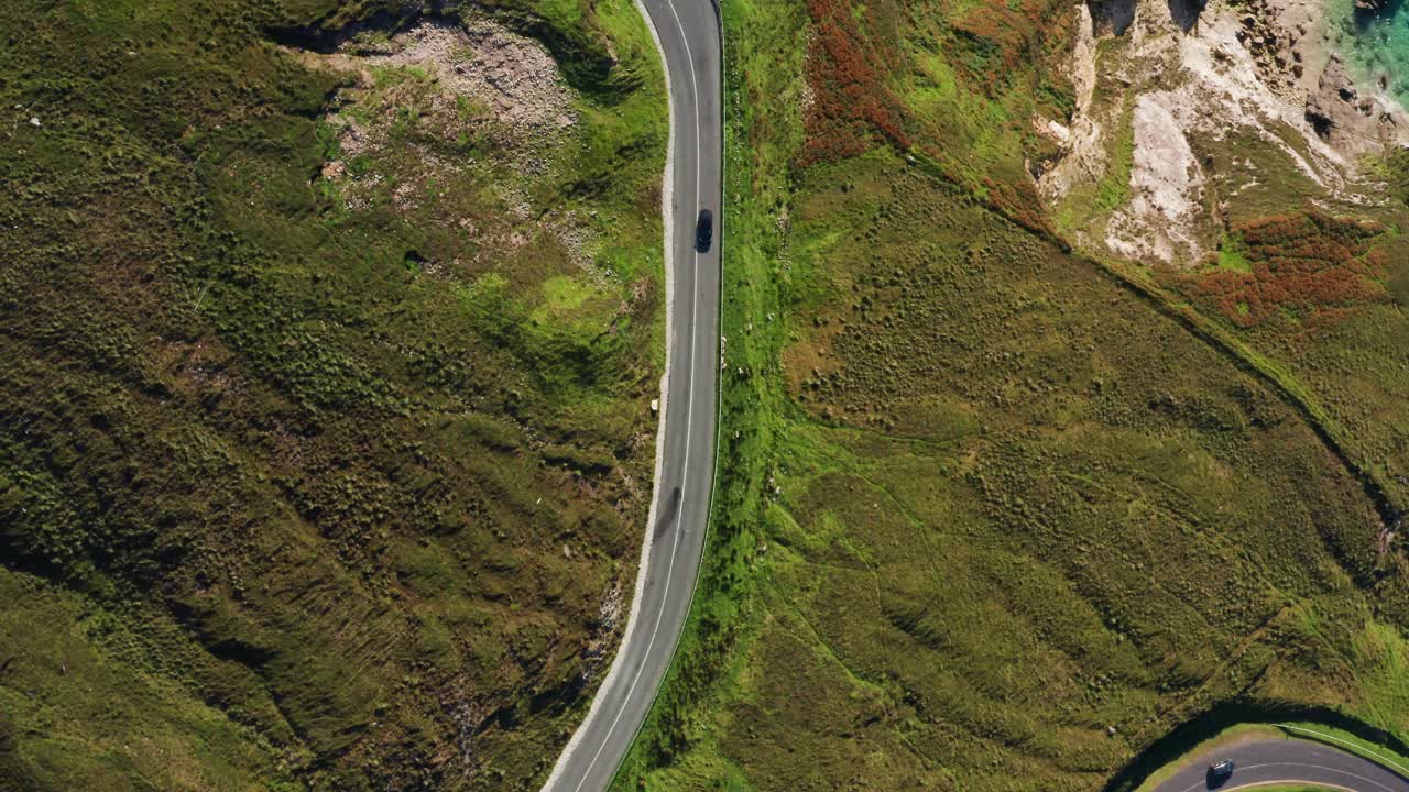 Aerial top-down flight over the winding mountain road with cars driving through the Achill Island’s grass-covered hills during a sunny day