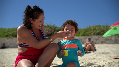 Slow-motion-of-a-mexican-latin-mother-wearing-a-swimsuit-cleaning-her-sons-nose-with-some-tissue-paper-at-the-beach-in-Mexico