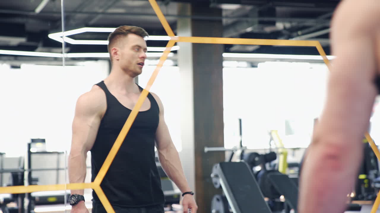 Sportsman in mirror reflection in fitness centre. Handsome athlete rests after hard training. Muscular bodybuilder indoors.